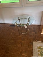 Side table with octagonal bevelled glass top shown from angled front view on parquet floor beneath window.