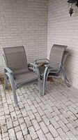 Two aluminum outdoor patio chairs with light grey frames and matching fabric seating placed outside on a brick patio.