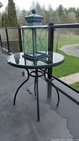 Outdoor round metal table with glass top and black metal frame on a deck