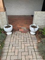 Two matching white concrete planters positioned near a brick porch step, showing overall shape and size.