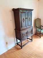 Full view of the solid oak Jacobean-style cupboard showing upper and lower sections with four etched glass doors and carved legs in a room