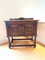 Front view of dark wood sideboard with carved Jacobean style doors and legs.