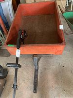 Front view of the metal yard trailer with red bed and black hitch arm, showing the handle or lever attached.