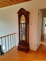 Full view of the tall, slim solid wood grandfather clock with glass door and visible pendulum weights.