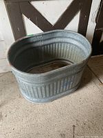Photo of galvanized steel water trough showing oval shape and ribbed sides against barn wall.