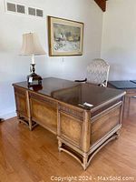 Full front view of executive desk showing polished wood surface, lamp on top, chair behind, carved trim, and recessed paneled sides.