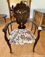 Front view of the carved oak armchair with removable embroidered cushion
