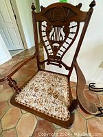 Full view of the antique Scandinavian wood carved armchair with needlepoint seat and carved wooden adornments, placed on tiled flooring.