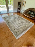 Full view of the Persian area rug spread on wooden floor in a bright room, showing white base with beige, brown, and green pattern.
