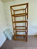 Full view of the solid rattan bookshelf showing the frame and two glass shelves in place; additional glass shelves stand wrapped beside it.