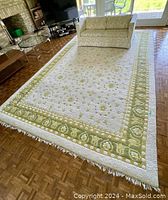 View of whole Persian handwoven rug featuring bright green patterned border and floral motifs in cream background under couch.