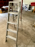 Full view of aluminum 4-step ladder standing open in garage with visible wear marks.