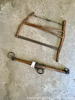 Vintage bow saw and drawknife fully visible on concrete floor.