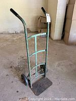 Side angled view of green metal hand cart dolly with two wheels and black rubber handles, showing flat loading plate.
