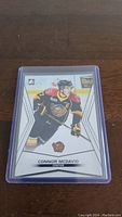 Photo of Connor McDavid rookie hockey card in black, red, and yellow jersey inside a protective plastic sleeve on a wooden surface.
