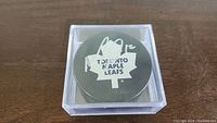 Top view of the Toronto Maple Leafs hockey puck with Mason Raymond autograph in silver ink and number '12' on top. Puck inside clear plastic display case.
