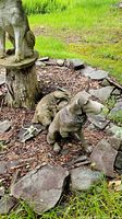 Two outdoor dog sculptures placed on earth and surrounded by stones, showing damage and weathering.
