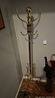 Full view of the brass colored metal coat rack showing height and base umbrella rings.