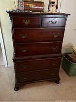 Front view of the wooden dresser with six drawers, showing scratches and scuffs and decorative items on top.