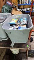 Large plastic bin on furniture dolly with various DVDs visible inside, showing general lot contents.
