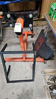 Orange engine stand with wheels and adjustable mounting plate alongside black engine cover on garage floor.