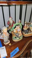 Photo showing multiple figurines including a musical couple with dogs and Santa Claus on a wooden shelf
