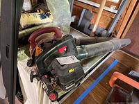Overview photo showing both gas blowers on a table in a wooden shed with some background tools and materials.