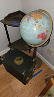Photo of the globe on wooden stand, a two-tiered wooden corner table, and a wooden carry case with visible wear.