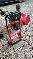 Front angle photo of the red and black adjustable hand truck, showing the metal frame, black handle, and wear on base plate.