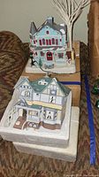 Photo of two ceramic holiday houses with Victorian architecture, snow on roofs, and holiday decorations including a snowman and tree