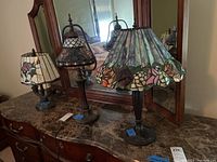 Set of 3 stained glass style table lamps on a wooden dresser in front of a mirror, showing their shades and bases
