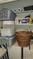 Multiple stacked plastic laundry baskets and a wicker basket on a shelf with some household items visible.