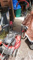Photo showing full view of red Craftsman lawn mower with black engine and handlebar on gravel floor, surrounding shed items visible.