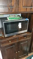 Panasonic microwave on wooden cabinet, showing whole unit and some kitchenware on top.