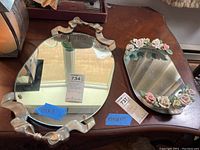 Photo showing two vanity mirrored trays on wooden surface, large tray with silver bow frame and smaller oval floral tray