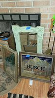 Three framed wall mirrors together against a fireplace and wall, showing size and style variety including the green frame and Busch logo mirror.