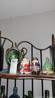 Full view of four Christmas music boxes on a shelf: ceramic Santa, nutcracker, Christmas tree, and green glass with metal music box.