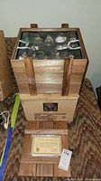 Full set of Thomas Pacconi Classic Christmas ornaments in wooden crate with fitted black foam insert, retail box below, and Certificate of Authenticity on floor in front.