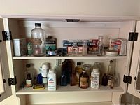 Full view of cabinet interior showing a collection of vintage apothecary and first aid bottles and containers on two shelves including glass bottles, tins, and small boxes.