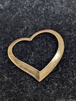 Close-up of the gold heart-shaped pendant on a black textured background, showing front view and smooth finish.