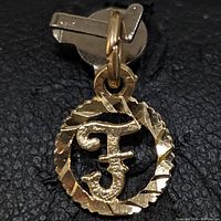 Close-up front view of the 10K yellow gold letter F pendant hanging on a pin backing, showing texture and twisted rope border.