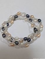 Photo showing the full coiled necklace with white, cream, and dark blue fresh water pearls interwoven in braided silver-tone chains.