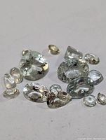 Photo showing a collection of multiple loose faceted aquamarine stones in different shapes and sizes, pale blue color, arranged on a white surface.