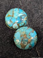 Two polished round turquoise gemstones with brown matrix on dark fabric background.
