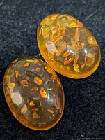 Photo of two polished oval amber gemstones with visible natural inclusions on a dark fabric background.