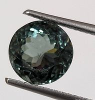 Round faceted gemstone held by tweezers, showing the top view and color details.