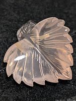 Close-up image of carved rose quartz leaf-shaped gemstone showing detailed etching and translucent pink color on dark background
