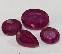 Four loose ruby gemstones arranged on white background showing various cuts and internal clarity.