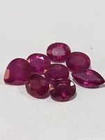 Seven genuine rubies in various cuts and vibrant red color arranged on a white background.