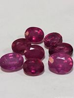 Seven loose genuine ruby gemstones arranged on white background, showing facets and color.